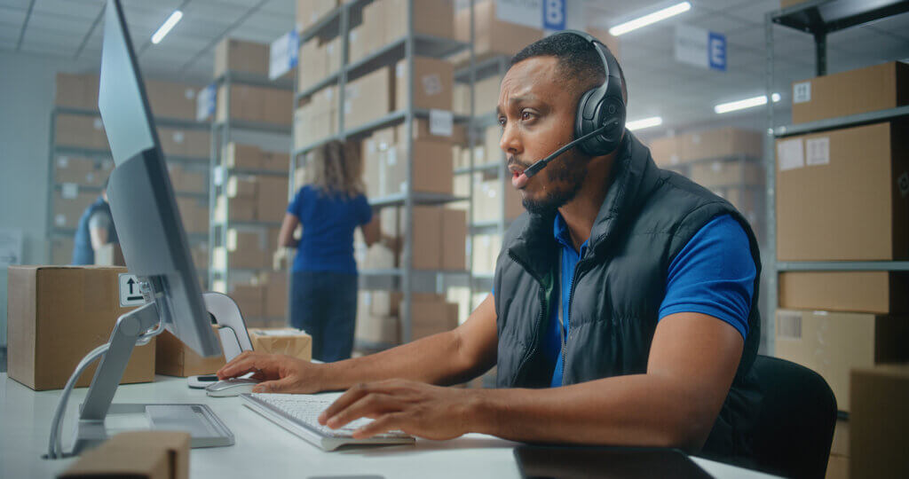 A man sitting at a computer wearing a headset is coordinating fleet asset management