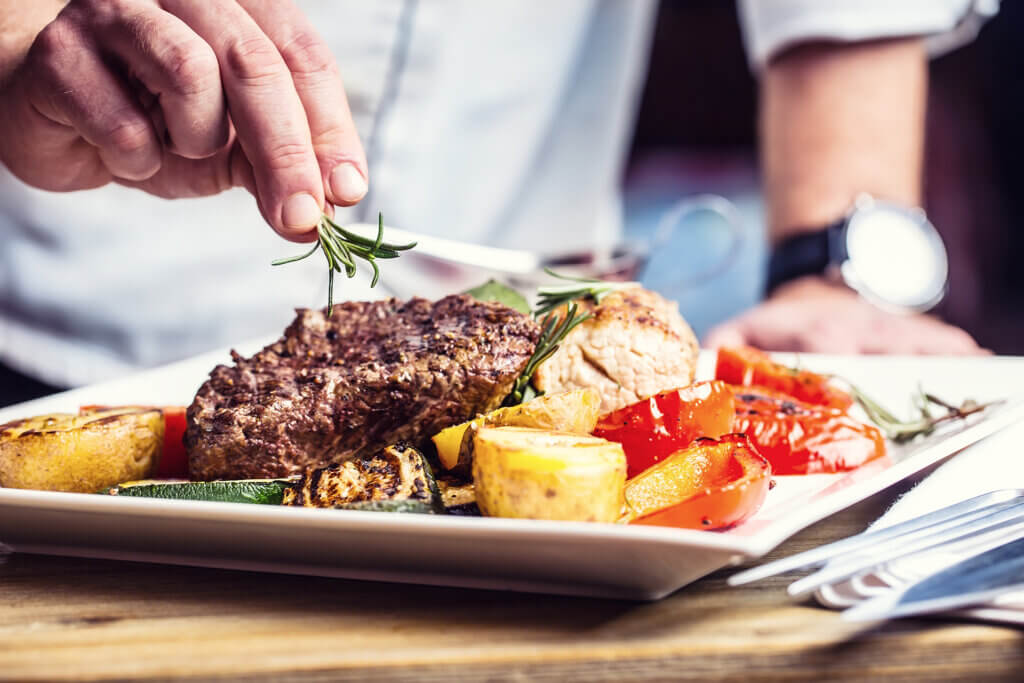 A chef is placing garnishes on a steak dish in a fine dining restaurant