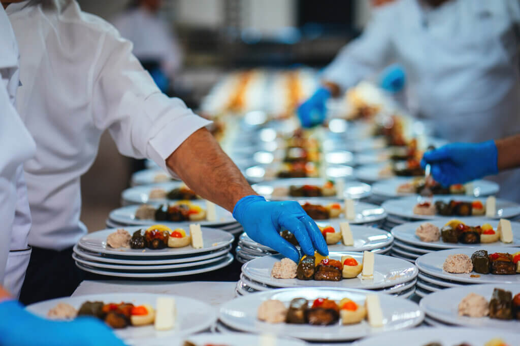 A long tables of small dishes being prepared by a catering company