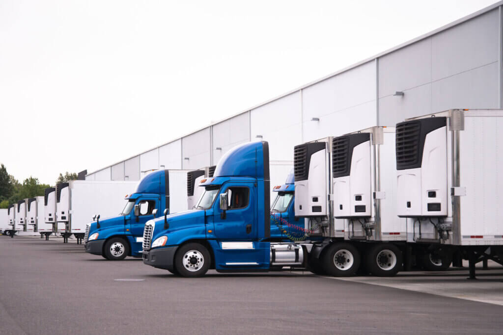 A line of semi trucks is parked outside of a warehouse providing distribution services