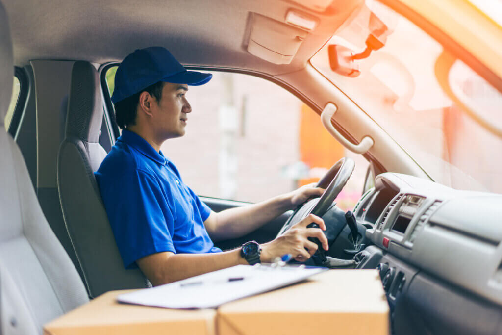 A male courier is driving with a package in the passenger seat of his car, providing reliable courier services