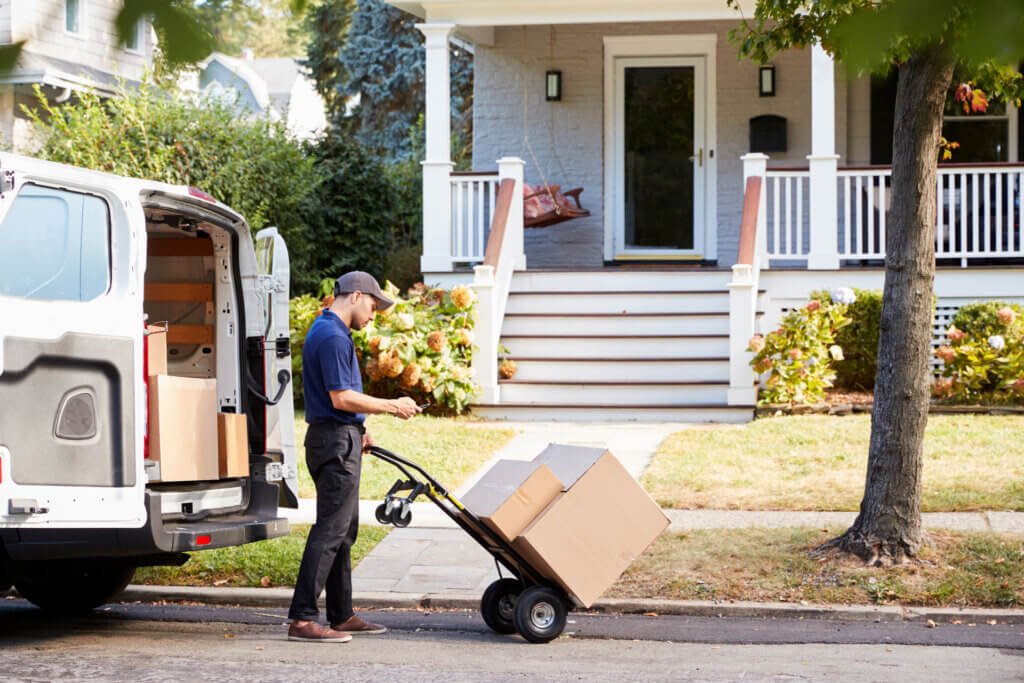 A courier is delivering boxes on a dolly to a residential home from an expedited shipping service
