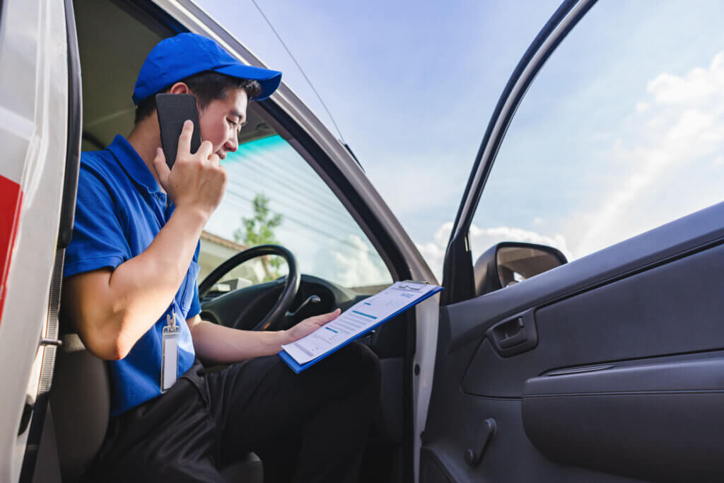 A delivery man is sitting on a van seat and calling a customer while on an independent courier job