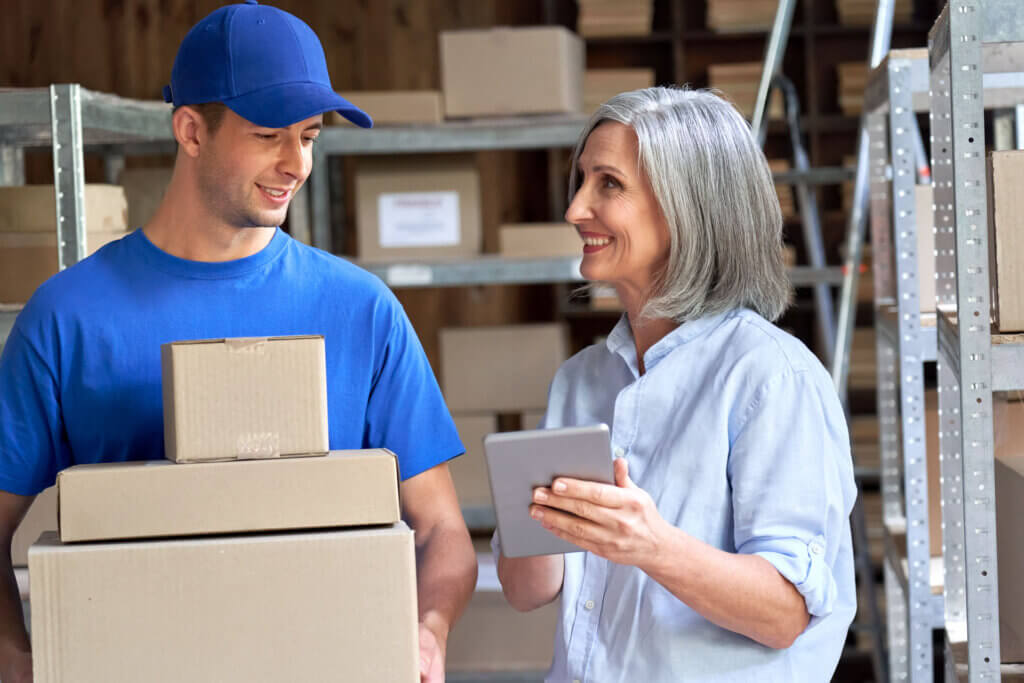 A woman is reviewing an expedited shipping order with a man who is holding three boxes