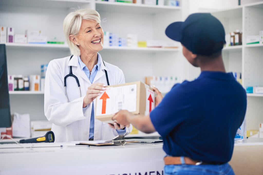 A courier is completing a routed delivery and handing a package to a healthcare worker