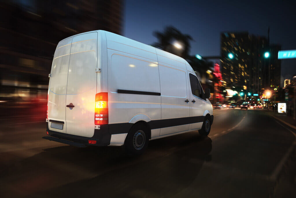 A white van providing a courier service is driving down a city street at night