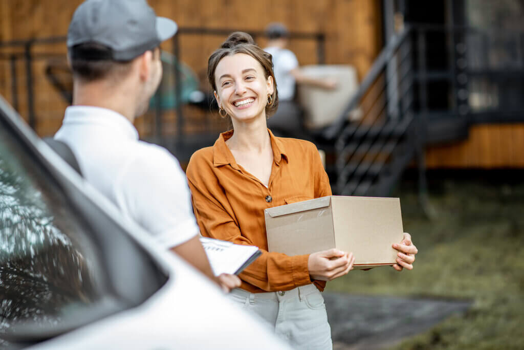 A woman standing outside of a business is accepting a package from a courier service